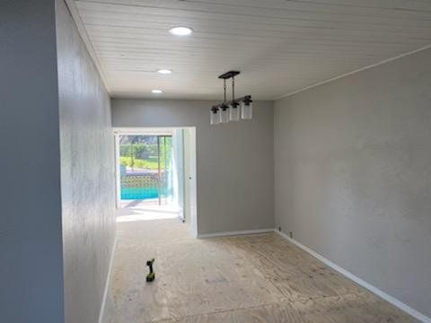 Freshly painted room mid-remodel with bare plywood subfloor, pool visible through the doorway.