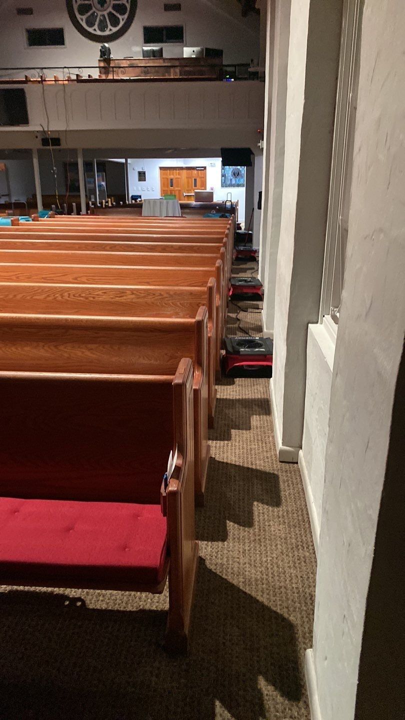 Industrial air movers and dehumidifiers running along the floor of a church sanctuary during water damage mitigation.